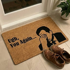 Doormat with a humorous design and text on a floor next to a door.