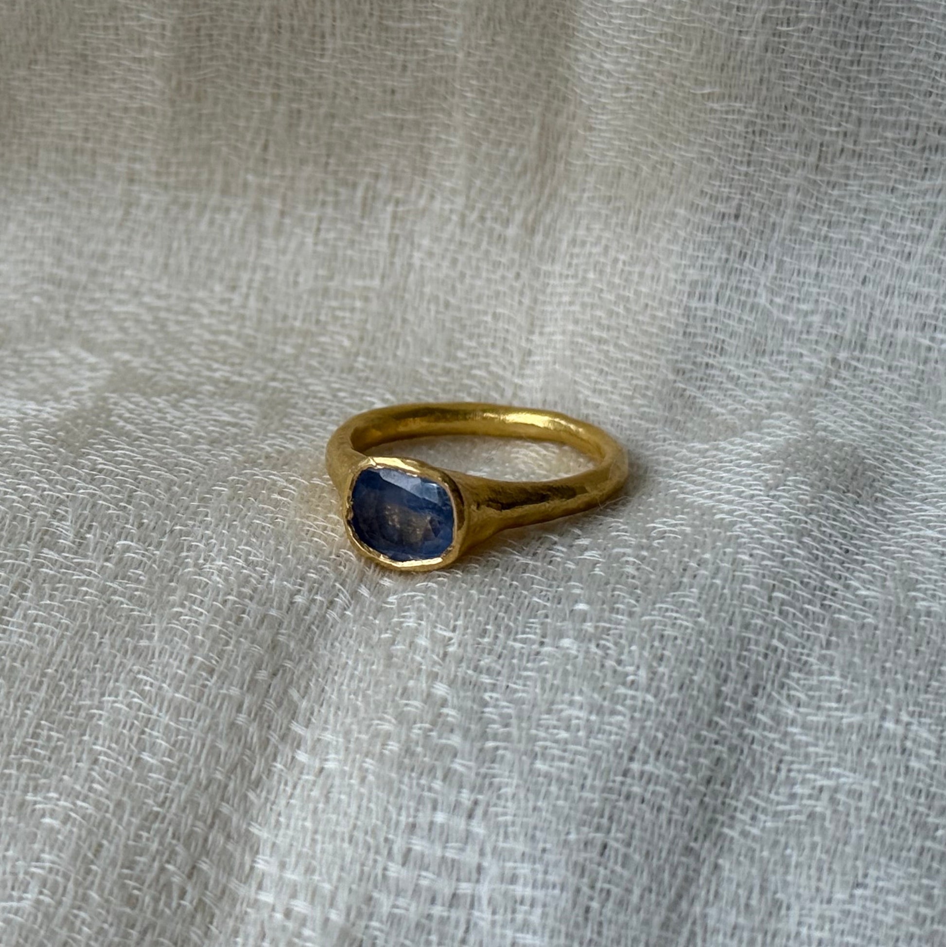 22ct Gold ring with a blue sapphire stone on a textured gray fabric background