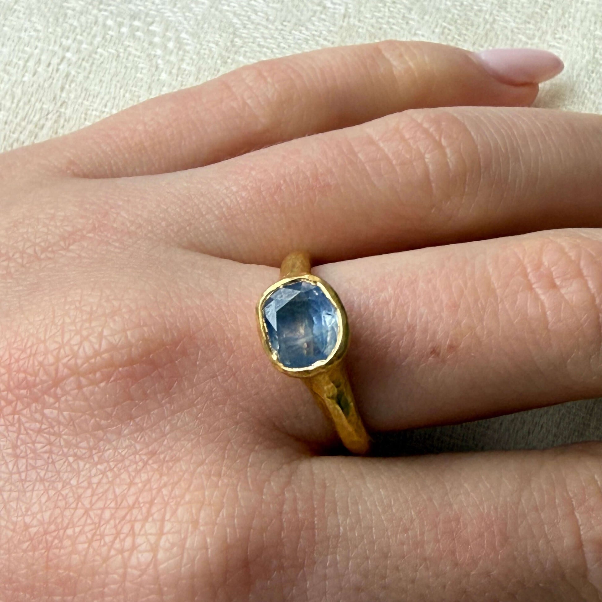 Gold ring with a blue gemstone on a finger against a neutral background