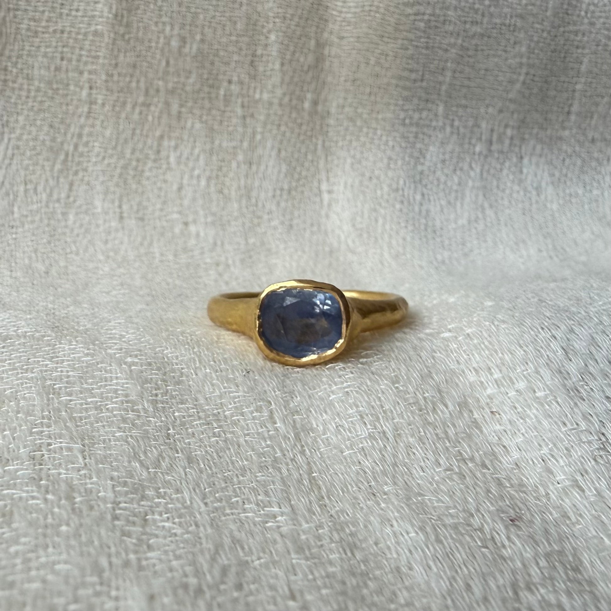 22ct Gold ring with a blue sapphire gemstone on a textured gray background