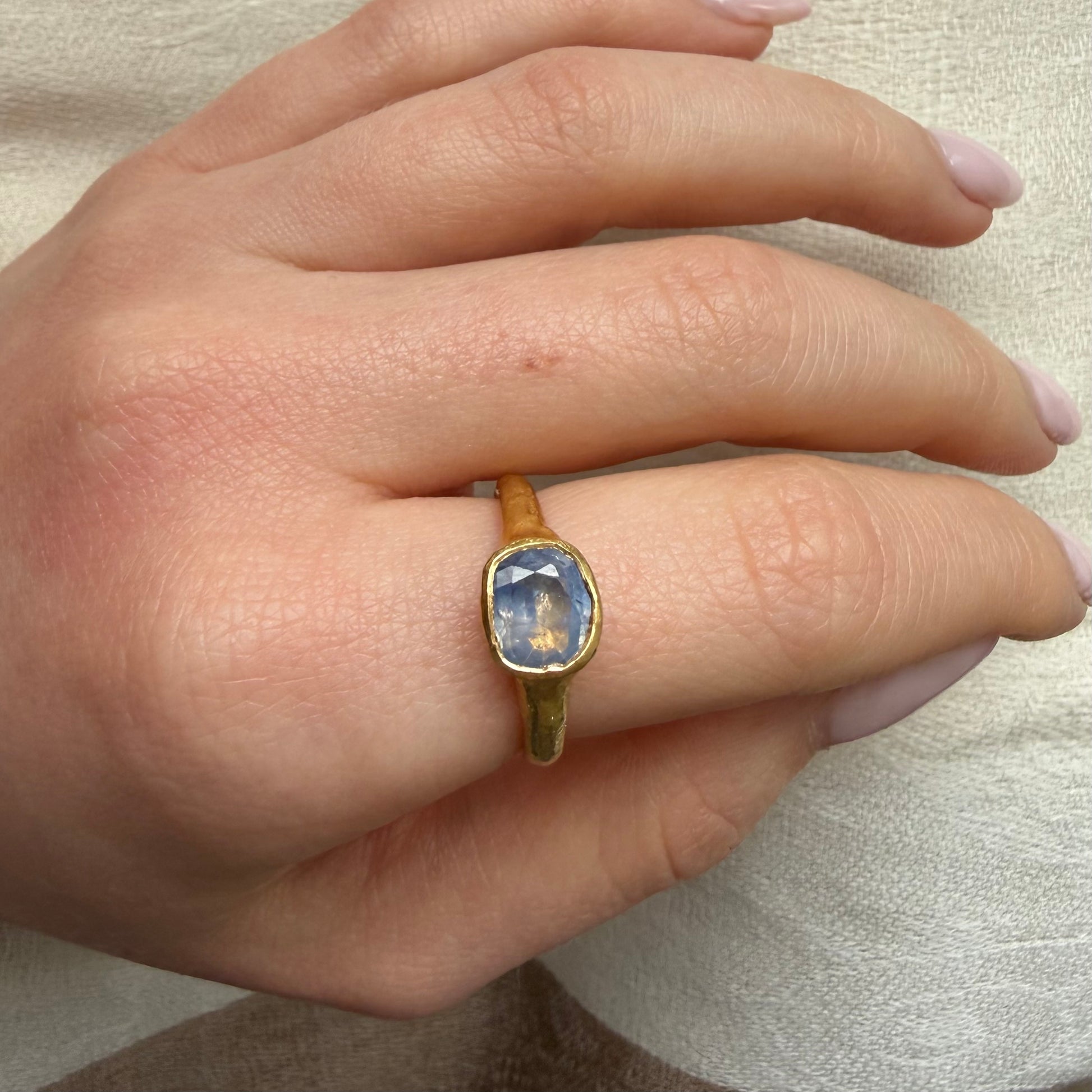 Gold ring with a gemstone on a person's finger against a neutral background