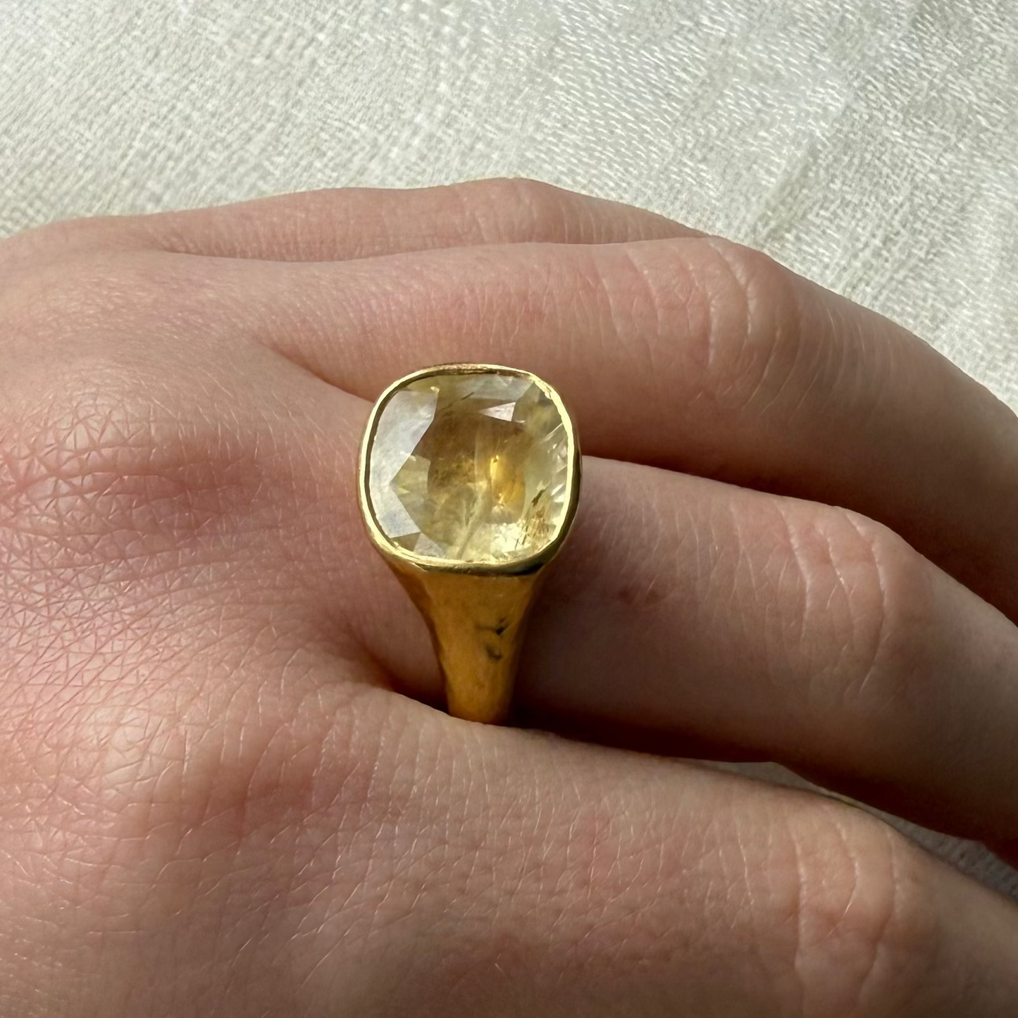 Hand wearing a 22ct solid gold ring with a large 8 carat yellow natural unheated gemstone on a light fabric background
