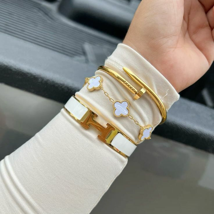 Close-up of a hand wearing multiple gold and white bracelets on a blurred background