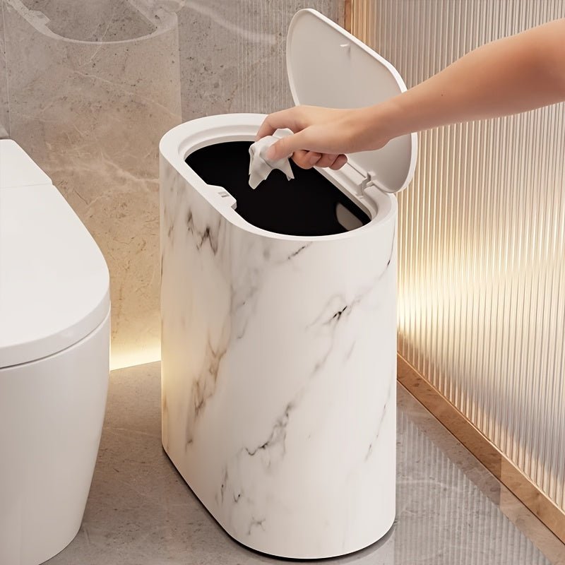 Person disposing of a tissue into a white marble-patterned trash can in a bathroom.