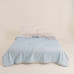 Light blue comforter on a bed with white pillows against a beige wall