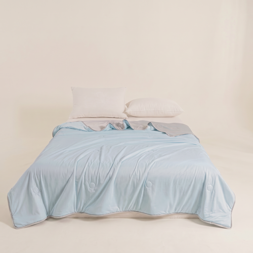 Light blue comforter on a bed with white pillows against a beige wall