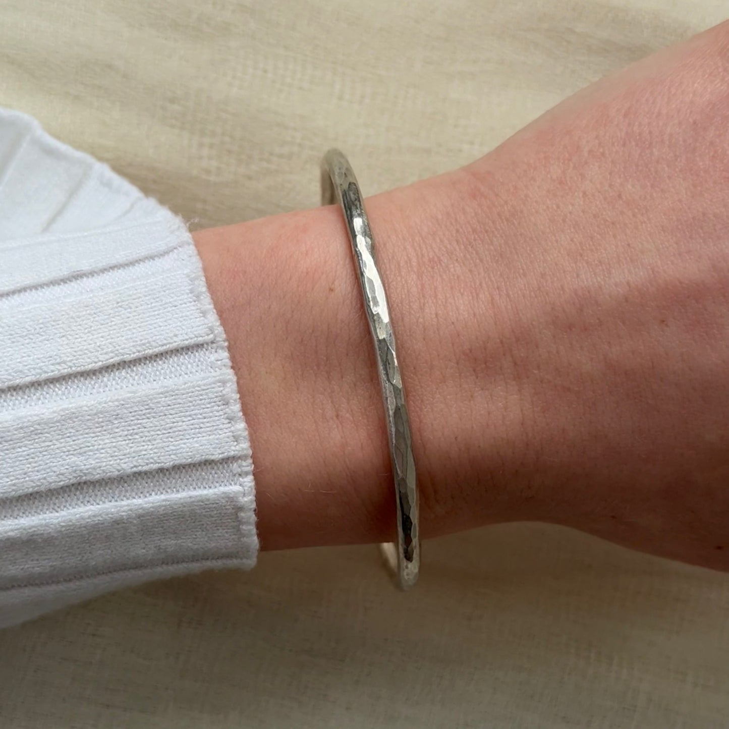 Silver bracelet on a wrist with a neutral background