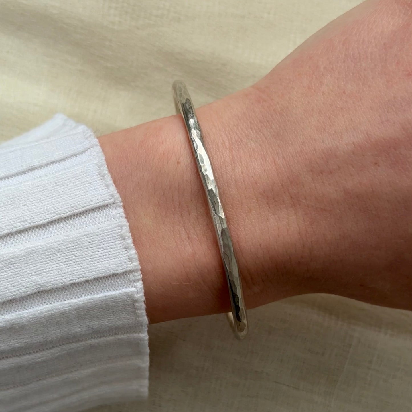 Silver bracelet on a wrist with a neutral background