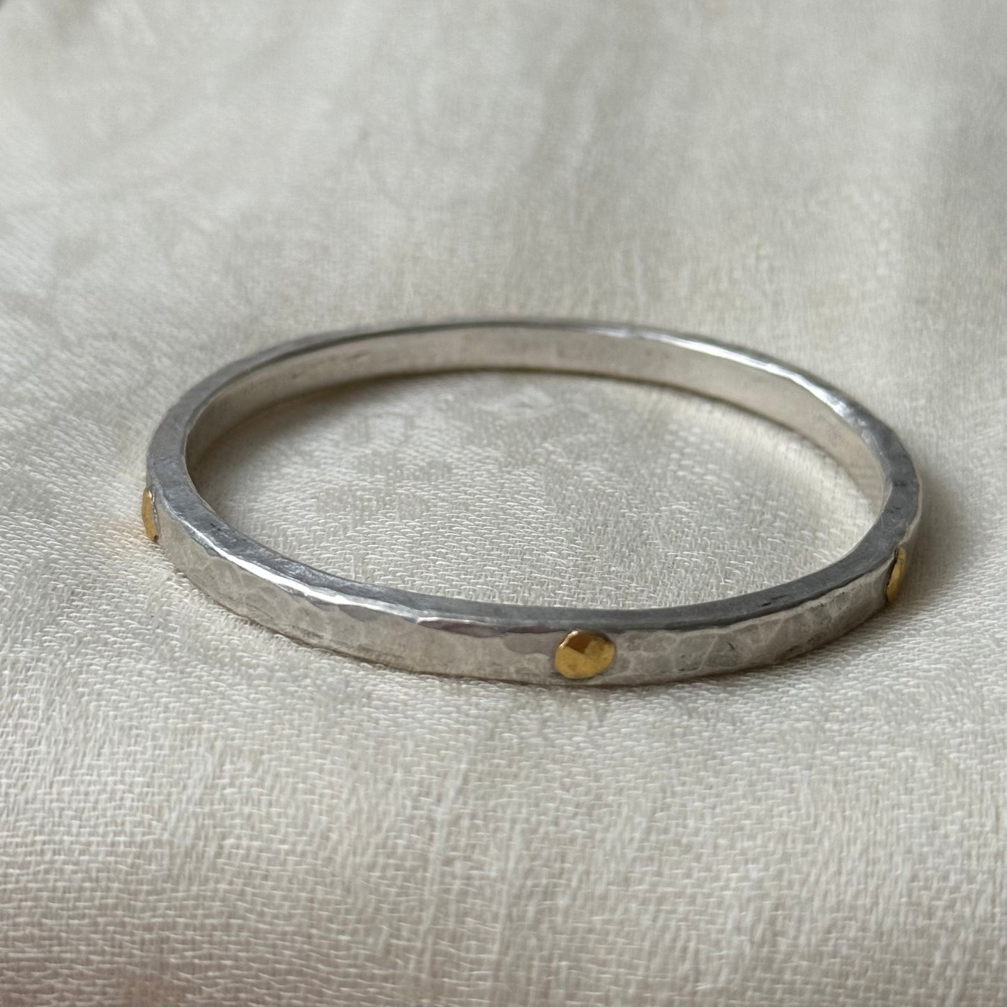 Silver bracelet with 22ct gold accents on a beige fabric background