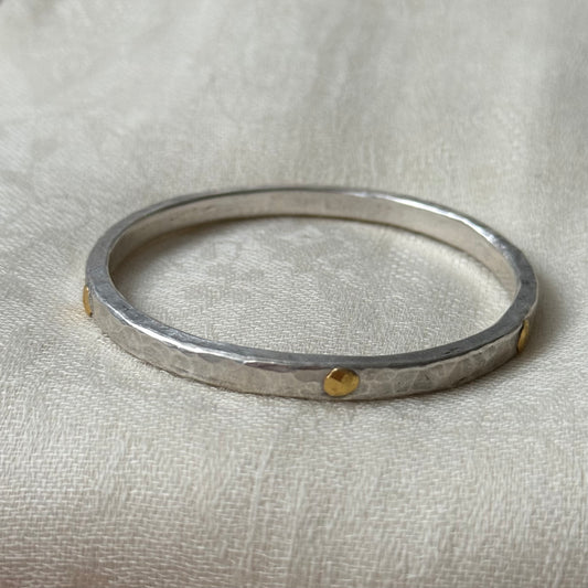 Silver bracelet with 22ct gold accents on a beige fabric background