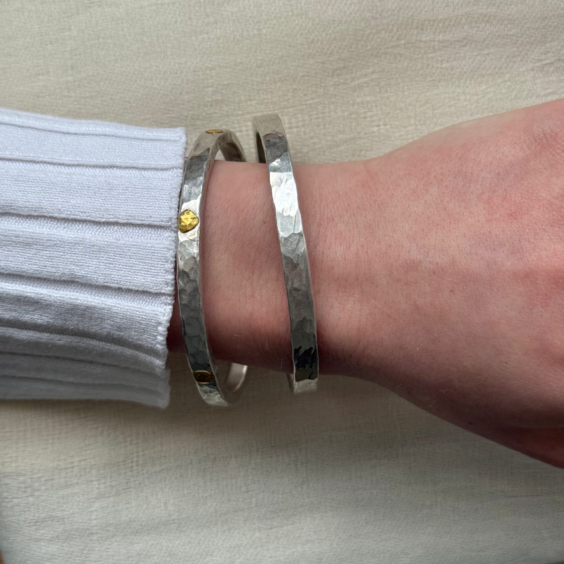 2 Silver bracelet with 22ct gold accents on a wrist against a beige background