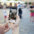Person holding a smartphone with a social media app open, blurred outdoor background