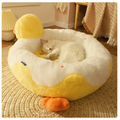 Cat lying on a yellow and white duck-shaped pet bed in a cozy room.