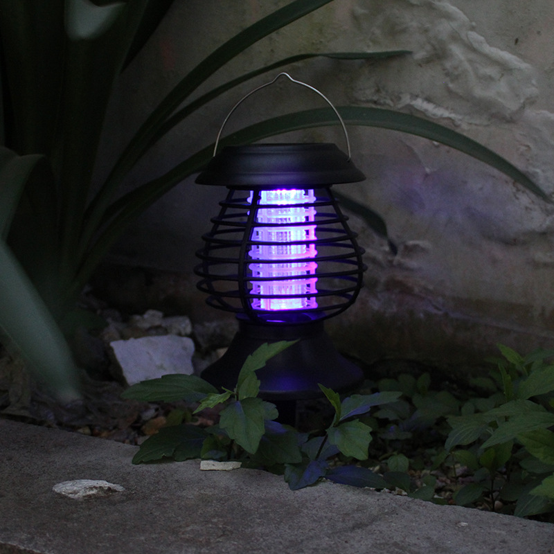 Solar mosquito zapper with purple light emitting on a plant and stone surface