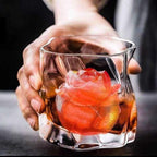 Glass with a red rose ice cube held by a hand against a dark background