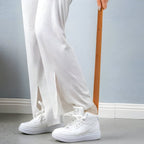 Person wearing white sneakers and light-colored pants against a gray background