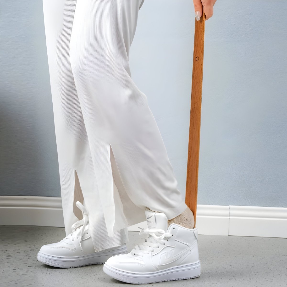 Person wearing white sneakers and light-colored pants against a gray background