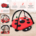 Red and black ladybug-shaped pet play mat with hanging toys on a beige carpet.