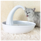 Cat drinking water from a white pet fountain on a soft surface.