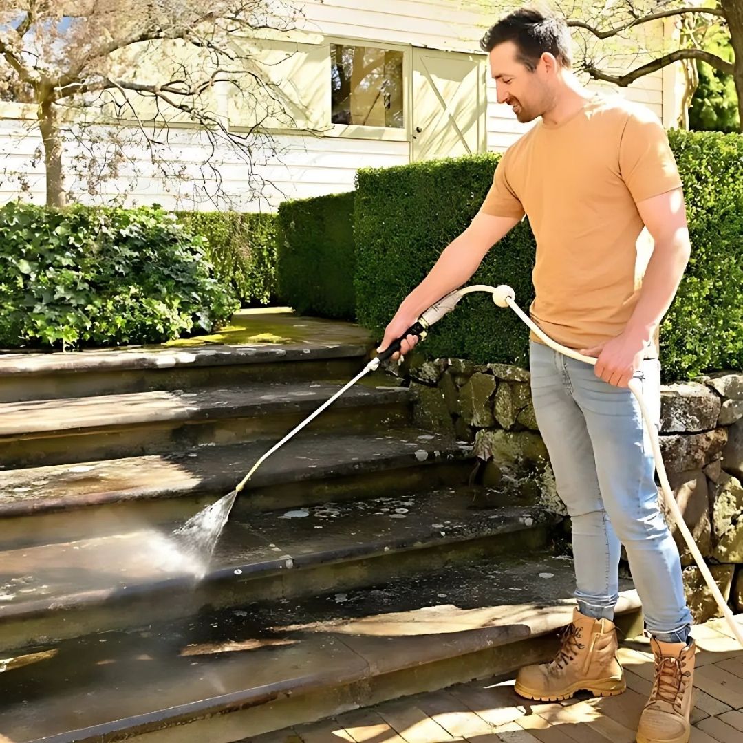 Man using a pressure washer to clean wooden steps outdoors.