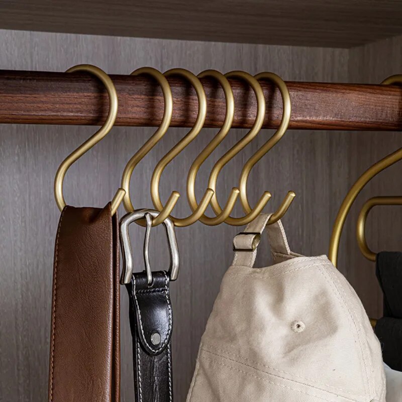 Gold hooks on a wooden rod with a belt and cap hanging from them against a neutral background.