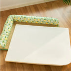 White foam mattress topper on a wooden floor with a decorative green border featuring lemon pattern.