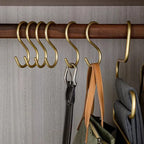 Gold hooks on a wooden rod with belts and bags hanging from them against a neutral wall.