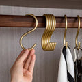 Gold hooks on a wooden rod with a hand holding one, against a neutral background.