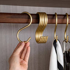 Gold hooks on a wooden rod with a hand holding one, against a neutral background.
