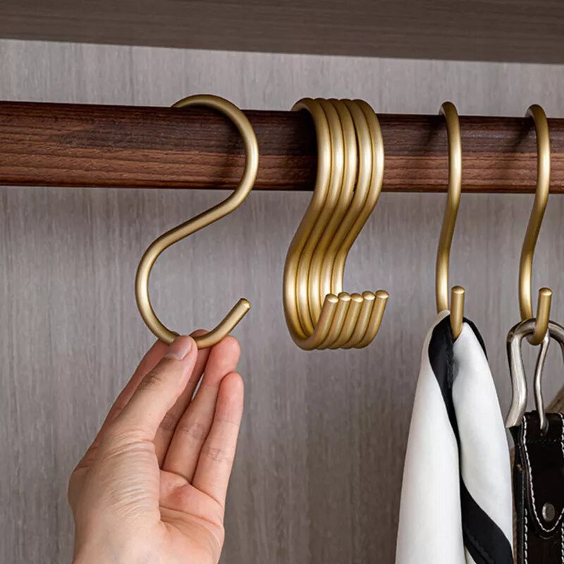 Gold hooks on a wooden rod with a hand holding one, against a neutral background.
