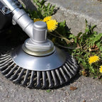 Close-up of a string trimmer cutting through weeds and dandelions on pavement.