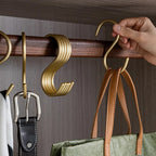 Hand holding a gold hook on a wooden rod with bags and belts hanging below.