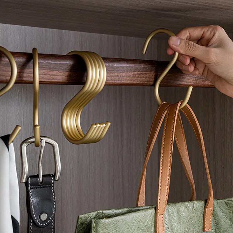 Hand holding a gold hook on a wooden rod with bags and belts hanging below.