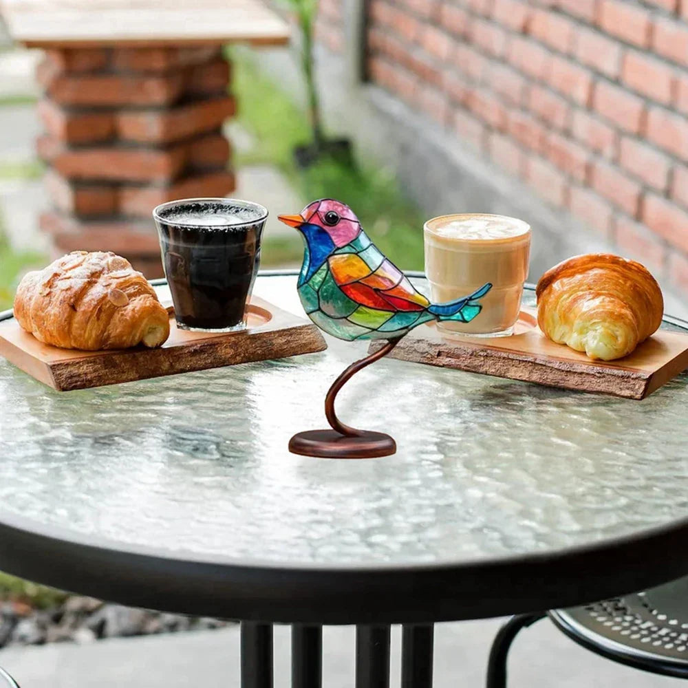 Colorful bird-shaped holder with a glass of black coffee and a cup of latte on a table outdoors.