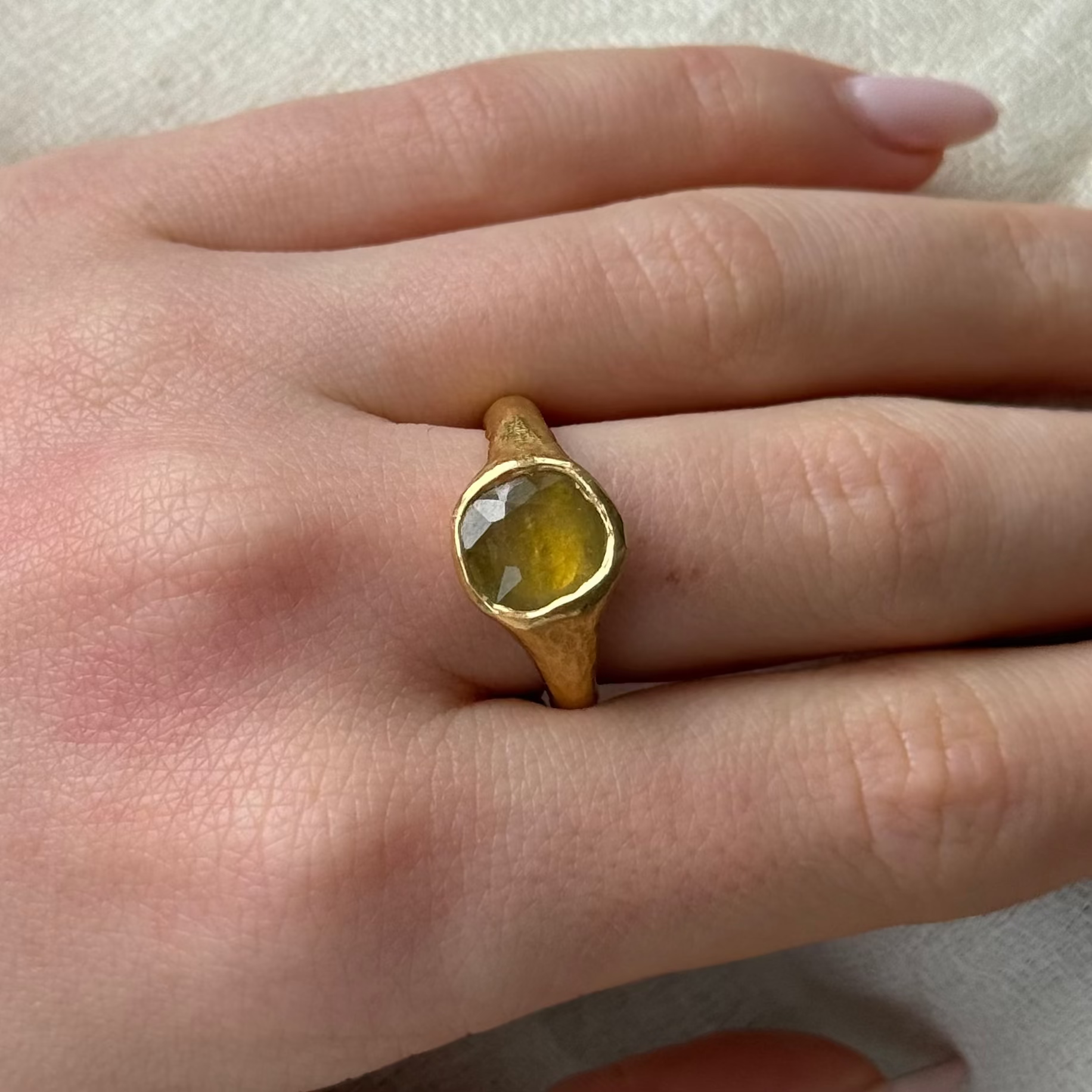 22ct Gold ring with a yellow sapphire gemstone on a person's finger against a neutral background
