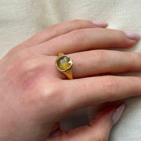 22ct Gold ring with a yellow sapphire on a hand against a neutral background