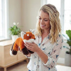 Woman holding a plush fox toy in a bright room with plants