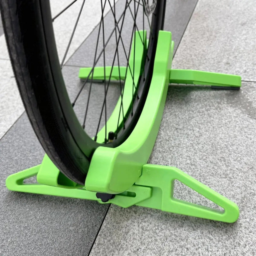 Green bike wheel truing stand holding a bicycle wheel on a tiled floor.